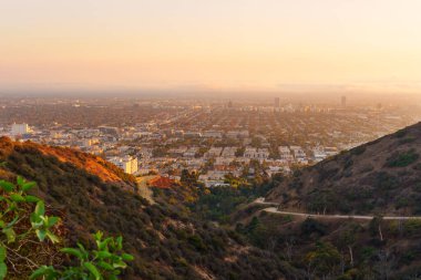 Runyon Canyon Parkı 'nda kıvrılan yürüyüş patikalarının manzarası gün batımında Los Angeles' ın canlı şehir manzarasını altın ışıklarıyla sergiliyor..