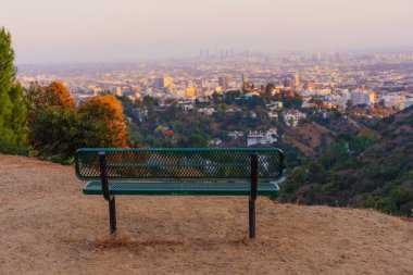 Tek başına yeşil bank Runyon Canyon Parkı 'nda toprak bir yolda uzanan altın saat boyunca uzanan Los Angeles ufkunun çarpıcı manzarasını sunuyor..