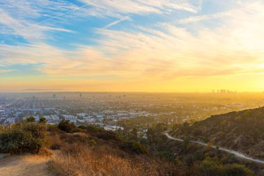 Runyon Canyon Parkı 'ndan canlı gün batımı manzarası. Yürüyüşçüler patikaları keşfediyor. Şehir silueti uzaktan görülebiliyor..