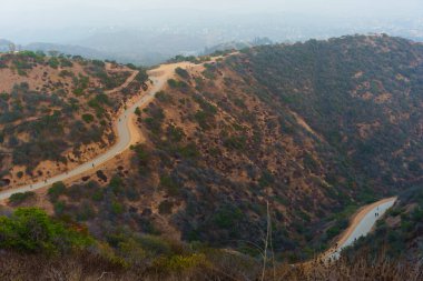 Los Angeles 'taki Runyon Canyon Parkı' ndaki dolambaçlı yürüyüş yolunun manzarası. Yol boyunca yemyeşil ve tepelerle çevrili sayısız yürüyüşçü var..