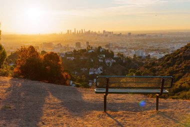 Los Angeles, California - 6 Ocak 2025: Los Angeles şehrinin Runyon Canyon Park 'taki ufuk çizgisini gösteren sakin günbatımı manzarası, şehir manzarasına bakan tek bir bank.