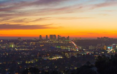 Los Angeles, Kaliforniya - 3 Aralık 2024: Gece vakti Los Angeles şehir merkezi muhteşem ateş renkli günbatımı gökyüzüne karşı bina ışıklarıyla parlıyor