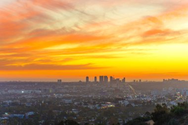 Los Angeles, Kaliforniya - 3 Aralık 2024: Los Angeles gün batımında gökyüzünde canlı turuncu ve pembe renklerin yer aldığı Runyon Canyon Park 'tan yakalanan gökyüzü ve şehir ışıkları parlamaya başlıyor..