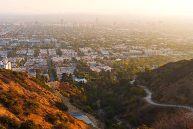 Los Angeles, California - 28 Kasım 2024 Runyon Canyon Parkı 'ndaki yamaçlar boyunca uzanan yılansı toprak yollara tepeden bakıldığında yürüyüşçüler bulutlu Los Angeles ufuk çizgisinde gün batımını izliyorlar..