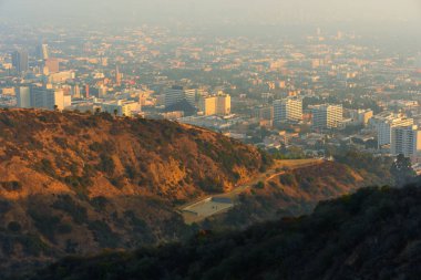 Los Angeles, Kaliforniya - 5 Aralık 2024: Runyon Canyon Parkı 'ndan geniş açılı manzara bir tenis kortunu gösteriyor ve Los Angeles şehir merkezine yayılıyor, doğa ile harmanlanmış kentsel yaşamı vurguluyor.