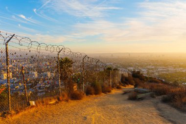 Los Angeles, Kaliforniya - 3 Aralık 2024: Sevginin özünü yakalamak için gün batımında Los Angeles siluetine karşı kurulmuş renkli aşk kilitleriyle bezenmiş bir çitin yakın görüntüsü.