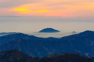 Sequoia Ulusal Parkı, Kaliforniya 'da gün batımında sisle kaplı bir dağ sırasının nefes kesici manzarası, gökyüzünde canlı renkler ve katmanlı arazi katmanları sergiliyor..