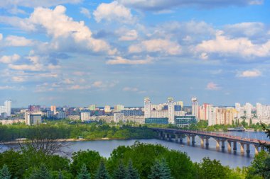 Kyiv, Ukrayna - 18 Mayıs 2025: Ukrayna 'nın Kyiv kentindeki Dinyeper Nehri' ni kapsayan Paton Köprüsü 'nün çarpıcı panoramik manzarası, canlı şehir siluetini ve açık mavi gökyüzü altında yemyeşil nehir kıyılarını gözler önüne seriyor.