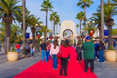 Los Angeles, Kaliforniya - 24 Aralık 2024: Los Angeles 'taki Universal Stüdyoları' nda parlak mavi bir gökyüzü altında kırmızı halıda yürüyen tatil süslemeleri ve kalabalıkları sergiliyor..