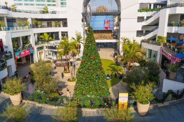 Los Angeles, Kaliforniya - 23 Aralık 2024: Bayram sezonu boyunca kalabalık bir Los Angeles alışveriş merkezinde festival dekorasyonları ve müşterilerle çevrili büyük bir Noel ağacının havadan görünüşü.