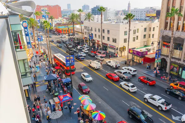 Los Angeles, Kaliforniya - 23 Aralık 2024: Şiddetli trafik, turistler, palmiye ağaçları ve renkli şemsiyelerin yer aldığı Los Angeles 'ta kentsel hayat dinamiklerini gözler önüne seren canlı sokak sahnesi.