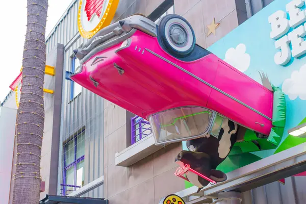 Los Angeles, California - 24 Aralık 2024: Mağaza vitrininde ters dönmüş gibi görünen pembe bir üstü açık araba kullanan bir ineğin yer aldığı mağaza önü heykeli.