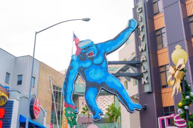 Los Angeles, Kaliforniya - 24 Aralık 2024: Universal CityWalk, Los Angeles 'ta bulunan ve bulutlu gökyüzü altında canlı renkler gösteren Noel Baba şapkası takan büyük mavi goril resmi.