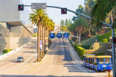Los Angeles, California - 23 Aralık 2024: Universal Stüdyoları Hollywood 'daki tramvay geçidi tabelasının görüntüsü, palmiye ağaçları, açık gökyüzü ve yakınlarda park edilmiş klasik bir tramvay.