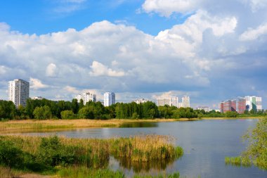 Geniş açılı çekim Kyiv 'de sakin bir göl yakalıyor. Arka planda bulutlu bir gökyüzünün altında modern binalar var..
