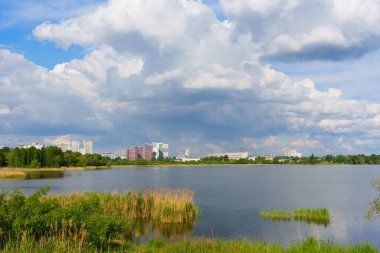 Sakin göl manzarası bulutlu gökyüzüne karşı modern binalar sergiliyor..