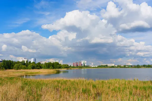Ukrayna 'nın Kyiv kentindeki sakin bir gölün geniş açılı görüntüsü, yemyeşil çimlerle çevrili ve mavi gökyüzü altında tüylü bulutlarla çevrili..