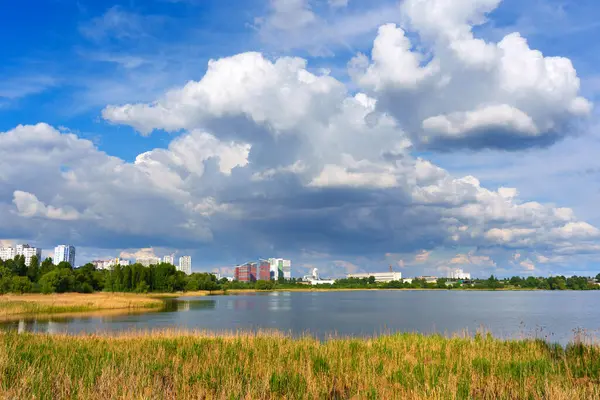 Yeşil bitki örtüsü ve dramatik bulutlarla çevrili sakin bir göle yansıyan binalarla Kyiv ufuk çizgisini net bir şekilde görebiliriz..