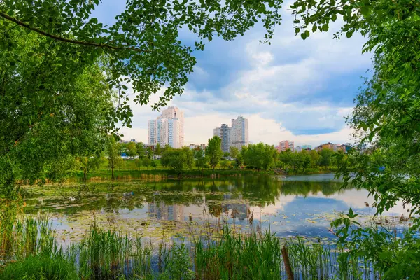 Bereketli yeşillik ve modern yerleşim binalarıyla çevrili sakin bir göl manzarası öğleden sonra saatlerinde parçalı bulutlu bir gökyüzünün altında..