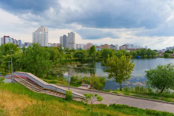 Kyiv, Ukrayna - 19 Mayıs 2025: Poznyaky Gölü ve Kyiv 'deki Poznyaky yerleşim bölgesinin manzarası, modern binalar, yeşillik ve bulutlu gökyüzünün altında sakin bir su yüzeyi.
