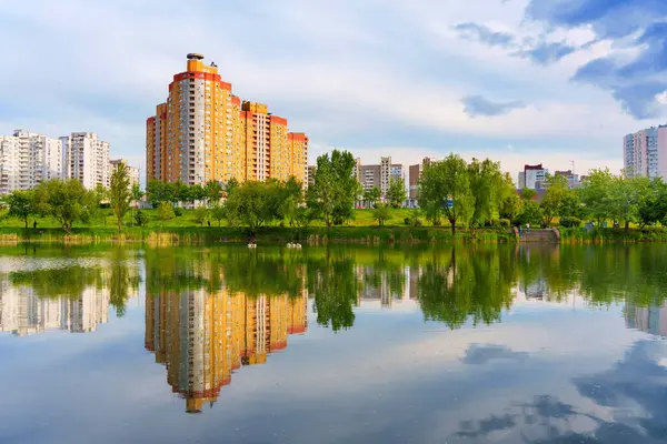 Kyiv, Ukrayna - 19 Mayıs 2025 Poznyaky, Kyiv 'de sakin göl, mavi gökyüzünün altındaki yerleşim binaları ve ağaçları yansıtıyor..