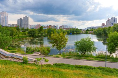 Kyiv, Ukrayna - 19 Mayıs 2025: Poznyaky Gölü 'nün sakin manzarası Kyiv' de parçalı bulutlu bir gökyüzünün altında yeşil ve meskun binalarla çevrili.