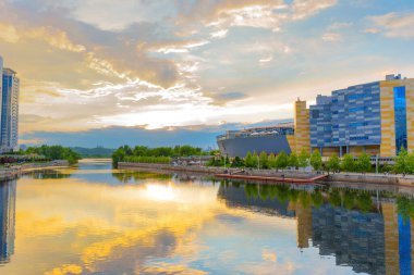 Kyiv, Ukrayna - 19 Mayıs 2025: Kyiv 'deki River Mall' ın sersemletici günbatımı manzarası, durgun suları yansıtıyor, canlı renkler ve modern mimariyi gözler önüne seriyor.