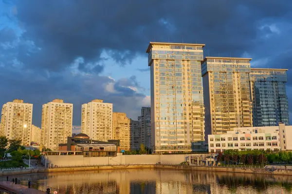 Kyiv, Ukrayna - 19 Mayıs 2025: Modern konut binaları ve River Mall, Kyiv 'deki yansıtıcı sular, üzerinde dramatik bulutlar bulunan altın saat boyunca.