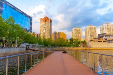 Kyiv, Ukrayna - 19 Mayıs 2025: Kyiv 'deki River Mall' da sakin nehir yolu, canlı bir gökyüzü altında modern binalar ve yemyeşil alanlar sergileniyor.