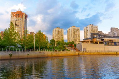 Kyiv, Ukrayna - 19 Mayıs 2025: Ukrayna 'nın Kyiv kentindeki bir nehir kıyısı boyunca modern yerleşim yerleri, sıcak günbatımı ışığı ile aydınlatılmıştır..