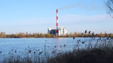 Gün boyunca sakin bir su kütlesinin atık yakma tesisi endüstriyel mimarisini ve çevresel etkisini vurguluyor..