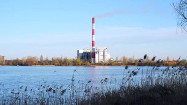 Kıyıda atık yakma tesisi görülebiliyor, uzun bir baca bacası duman yayıyor, atık yönetimi ve çevresel etki kavramını yansıtıyor.