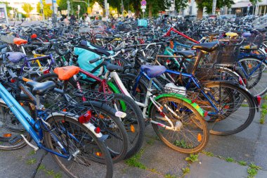 Heidelberg, Almanya - 21 Haziran 2025: Gün batımında hareketli bir şehir merkezinde park etmiş yoğun bisiklet kümesi, motosikletlerden yansıyan akşam ışığını yakalıyor.