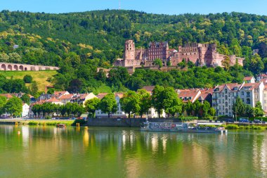Heidelberg, Almanya - 21 Haziran 2025: Heidelberg Kalesi 'nin geniş açılı manzarası bir tepenin üzerine tünemiş, Neckar Nehri' ne yansımış, canlı yeşillik ve açık mavi gökyüzünü göstermektedir..