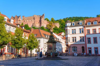 Heidelberg, Almanya - 21 Haziran 2025: Heidelberg 'de tarihi binalar ve tepedeki Heidelberg Şatosu' nun yer aldığı canlı bir meydanın geniş açılımı.