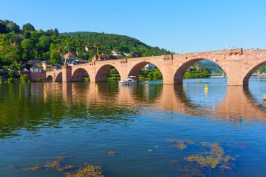 Almanya 'nın Heidelberg kentindeki tarihi Köprü manzarası, Neckar Nehri' ni kaplıyor, berrak sularda ve çevreleyen yeşilliklerde yansımalar var..