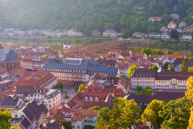 Almanya, Heidelberg 'in tarihi mimarisi, yumuşak sabah ışığı altında nehir ve köprüyü sergiliyor..