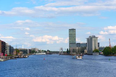 Berlin, Almanya - 30 Mayıs 2025: Berlin 'deki Spree Nehri' nin geniş açılı görüntüsü kıyıdaki modern binaları parlak, parçalı bulutlu bir gökyüzü altında sergiliyor.
