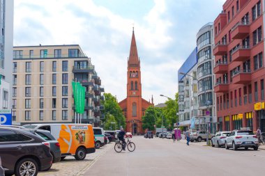 Berlin, Almanya - 31 Mayıs 2025: Çağdaş binalar ve park halindeki arabalarla Berlin 'deki On İki Havari Kilisesi' nin geniş açılı görüntüsü, bulutlu bir günde şehir yaşamını gözler önüne seren.