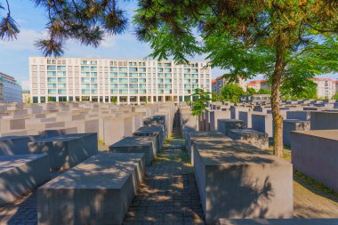 Berlin, Almanya - 31 Mayıs 2025: Berlin 'de öldürülen Avrupa Yahudilerinin anısına, arka planda çağdaş binalarla tezat oluşturan mavi gökyüzü altında gri beton levhalar yer alıyor..