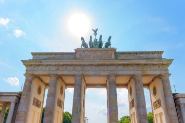 Berlin, Almanya - 31 Mayıs 2025: Tarihi bir anıt olan Brandenburg Kapısı, klasik mimari, parlak güneş ışığı ve ikonik heykel ve sütunlarını aydınlatan açık mavi bir gökyüzüne sahiptir..