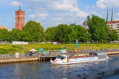 Berlin, Almanya - 31 Mayıs 2025: Berlin 'in ikonik mimarisi, yemyeşil ve canlı şehir yaşamının yer aldığı Spree Nehri üzerinde gün ışığında gezinen eğlence teknesi.
