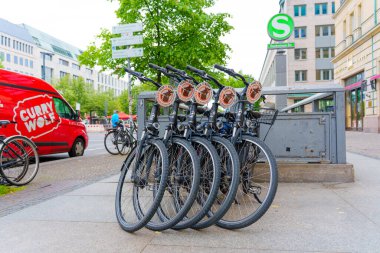 Berlin, Almanya - 1 Haziran 2025: Bisikletler Berlin, Almanya 'da renkli bir Currywurst yemek kamyonunun yanına dizildi. Arka planda yeşil ağaçlar ve şehir mimarisi olan şehir merkezi.