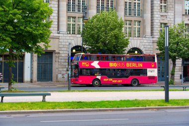 Berlin, Almanya - 1 Haziran 2025: Büyük Otobüs Berlin tur otobüsü tarihi bir binanın yakınına park edilmiş. Bereketli yeşil ağaçlar, açık mavi gökyüzünün altında şehir yaşamını gözler önüne seriyor..