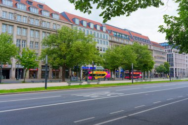 Berlin, Almanya - 1 Haziran 2025: Berlin 'de renkli çift katlı otobüsler ve huzurlu kentsel atmosfer içeren canlı ağaçlar ve modern binalarla dolu bir cadde.