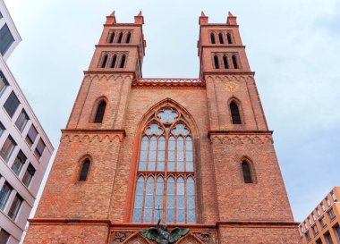 Berlin, Almanya - 1 Haziran 2025: Berlin 'deki Friedrichswerder Kilisesi' nin mimari ayrıntıları kırmızı tuğlalar, ikiz kuleler ve bulutlu gökyüzü altındaki Gotik unsurlar kentsel çevreyi yansıtıyor.