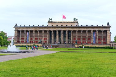 Berlin, Almanya - 1 Haziran 2025 Berlin, Almanya 'da bulutlu bir gökyüzüne karşı yemyeşil çimenler, ziyaretçiler ve bir çeşmeyle Altes Müzesi' nin etkileyici cephesi.