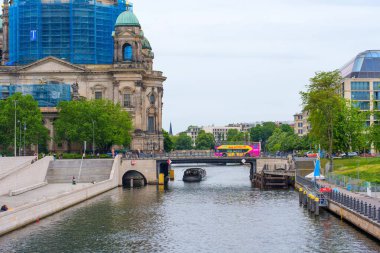Berlin, Almanya - 1 Haziran 2025: Spree Nehri 'nin yanındaki Berlin Katedrali' nin görüntüsü, parçalı bulutlu bir gökyüzü altında mimari ayrıntılar, yeşillik ve kentsel faaliyet sergilenmektedir..