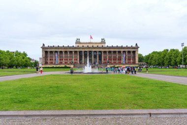 Berlin, Almanya - 1 Haziran 2025: Merkezi bir çeşme, yemyeşil yeşillik ve Berlin, Almanya 'daki açık alandan keyif alan ziyaretçilerin yer aldığı Altes Müzesi tarihi mimari görünümü.