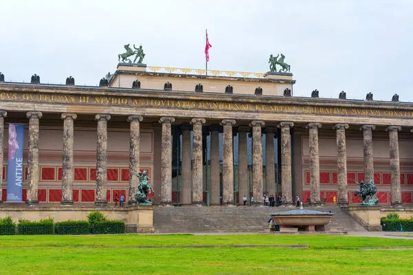 Berlin, Almanya - 1 Haziran 2025: Berlin 'deki Altes Müzesi' nin ön cephesinde bulutlu bir gökyüzüne karşı klasik sütunlar, heykeller ve canlı bayraklar yer alıyor, neoklasik mimariyi vurguluyor.